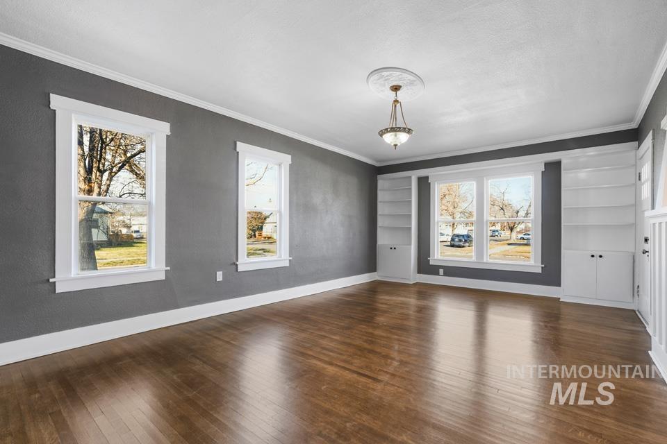 253 West Court Street Weiser, ID 83672 - Photo 4 of 35 Empty room featuring built in shelves, dark wood finished floors, and ornamental molding