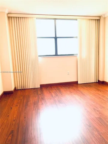 an empty room with wooden floor and windows with curtains