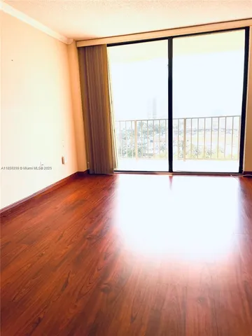 an empty room with wooden floor and windows with curtains