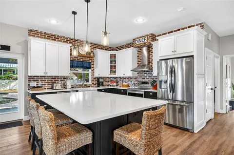 a kitchen with stainless steel appliances granite countertop a refrigerator a sink dishwasher a stove and white countertops with wooden floor