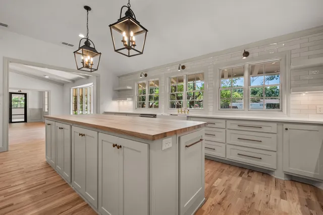 a open hall with wooden floor a chandelier a wooden table and chairs