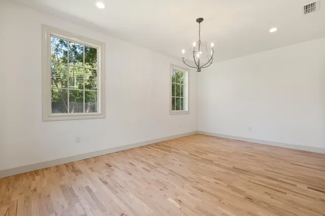 an empty room with wooden floor chandelier and windows