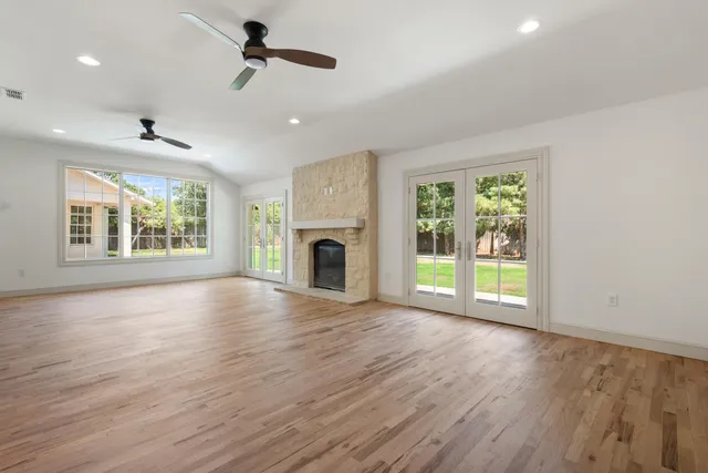 an empty room with wooden floor fireplace and windows