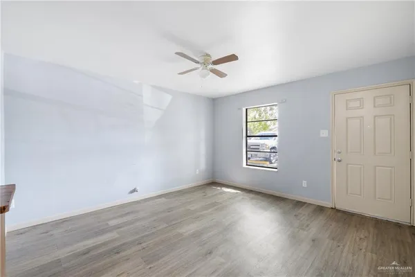 an empty room with wooden floor ceiling fan and windows