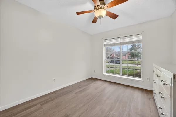 an empty room with wooden floor fan and windows