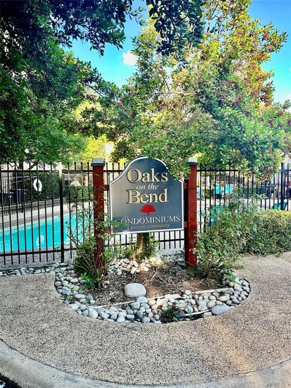 7340 Skillman Street, Unit 405 Dallas, TX 75231 - Photo 17 of 18 Community sign for "Oaks on the Bend Condominiums" featuring a black wrought iron fence, a rock garden, and mature trees