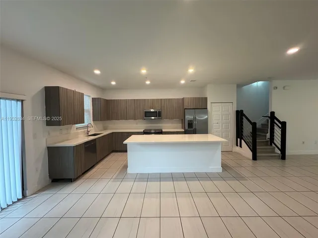 a large white kitchen with kitchen island a sink a counter top space and stainless steel appliances