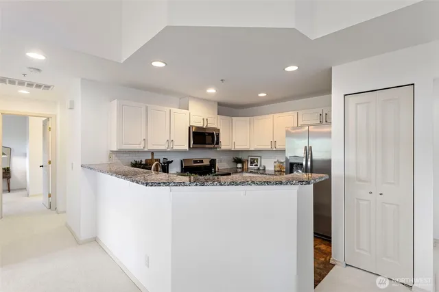 a kitchen with stainless steel appliances granite countertop a refrigerator a sink and white cabinets
