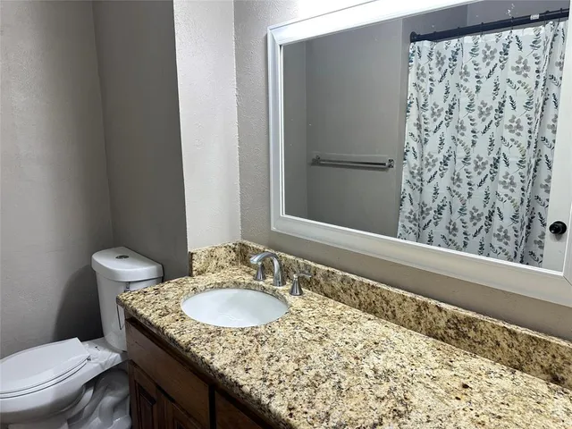 a bathroom with a granite countertop sink and a toilet