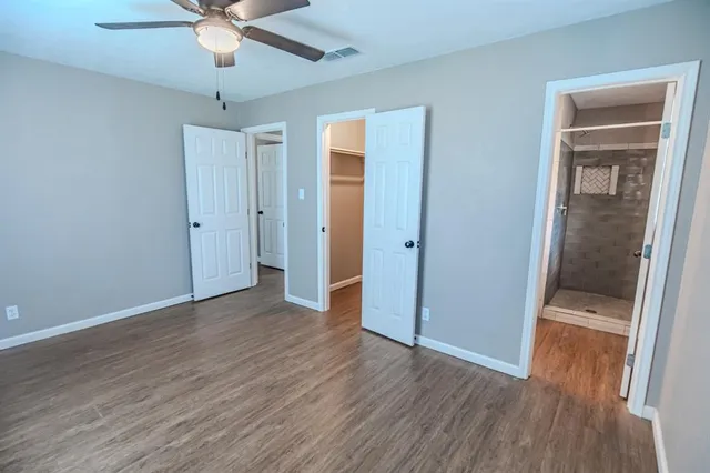 an empty room with wooden floor fan and windows