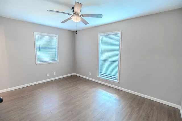 an empty room with wooden floor chandelier fan and windows