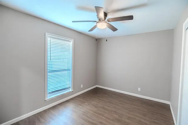 an empty room with wooden floor fan and windows