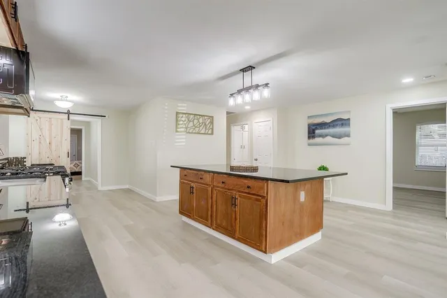 a large white kitchen with stainless steel appliances granite countertop a stove a sink a refrigerator and white cabinets with wooden floor