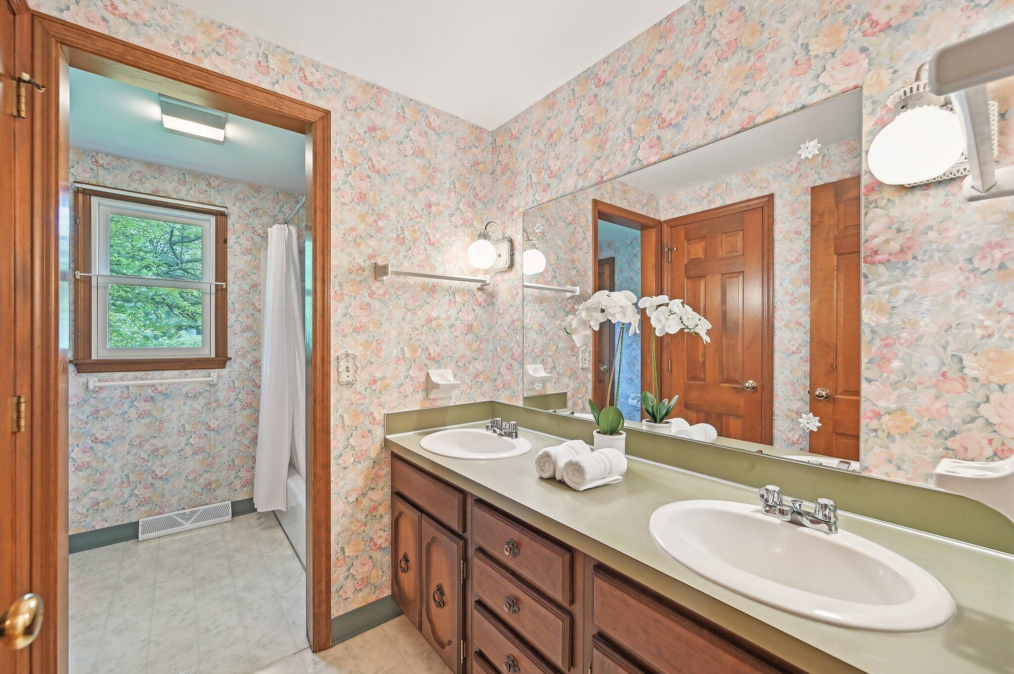 5917 Rocky Rill Road Columbus, OH 43235 - Photo 31 of 47 Full Bathroom This shared full bath features a dual-sink vanity with a large mirror, vintage floral wallpaper, and updated lighting. A door leads to a separate shower/tub area, offering privacy and convenience.