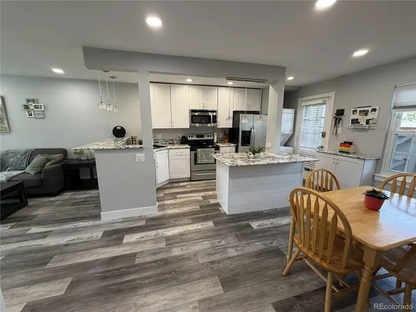 a room with stainless steel appliances kitchen island granite countertop a dining table chairs and a refrigerator