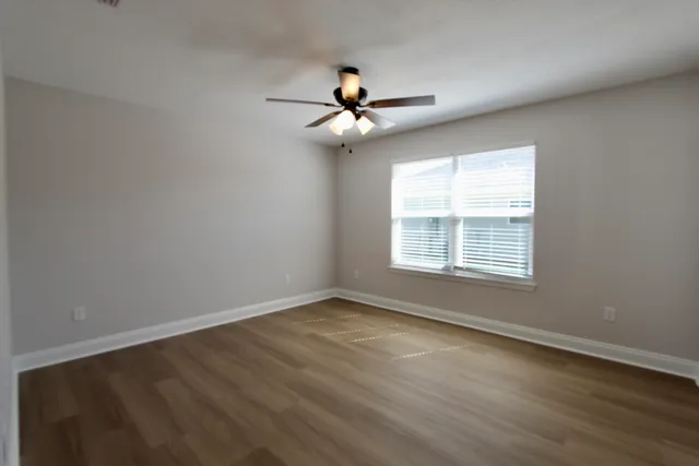 an empty room with wooden floor ceiling fan and windows
