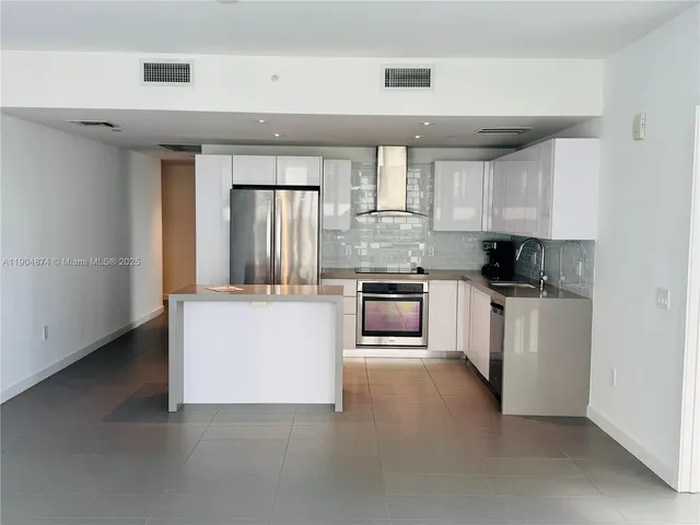 a kitchen with stainless steel appliances granite countertop a stove top oven a refrigerator a sink and dishwasher with white cabinets