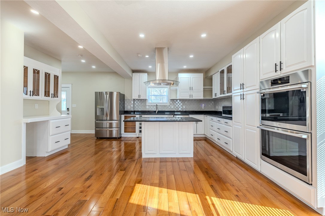 3516 Broadview Road Cleveland, OH 44109 - Photo 12 of 42 Kitchen with backsplash, glass insert cabinets, light wood-style flooring, island range hood, and stainless steel appliances