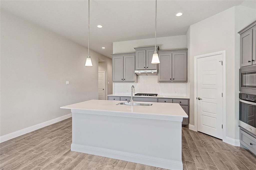 2217 Yellowhammer Road Denton, TX 76205 - Photo 15 of 30 a kitchen with kitchen island a stove a sink and a refrigerator with wooden floor