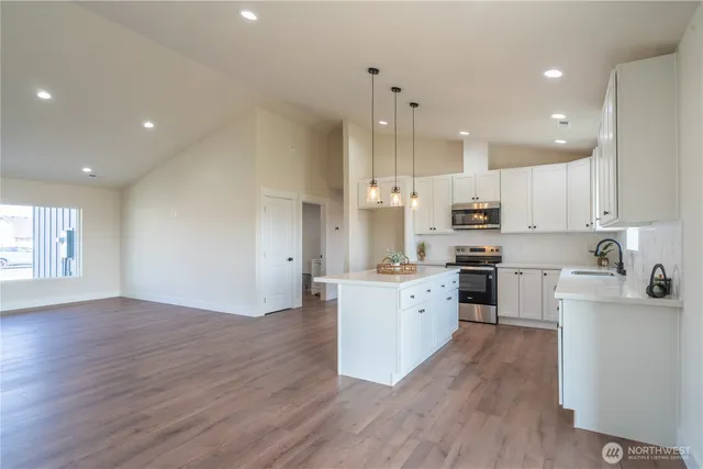 a kitchen with granite countertop a stove top oven a sink a refrigerator and white cabinets with wooden floor