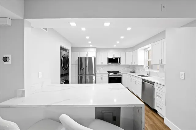 a large white kitchen with stainless steel appliances kitchen island a stove a sink a refrigerator and white cabinets