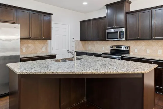 a kitchen with granite countertop stainless steel appliances a sink stove refrigerator and cabinets