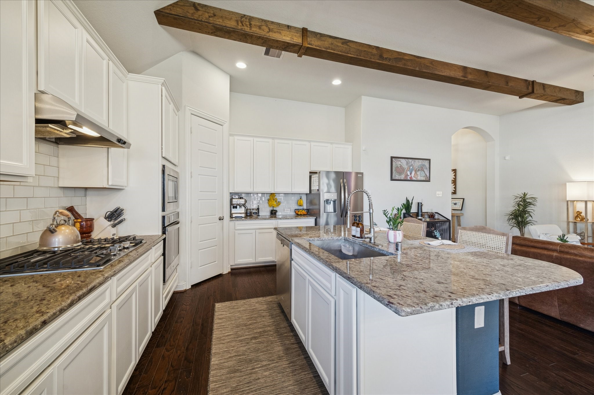 25214 Dewstone Way Porter, TX 77365 - Photo 9 of 29 The wood beams extend all the way into the kitchen. Granite countertops for style and durability. The island has bar seating and a convenient placement for a sink. Gas stove cooktop and a wall oven and microwave for luxury and functionality.