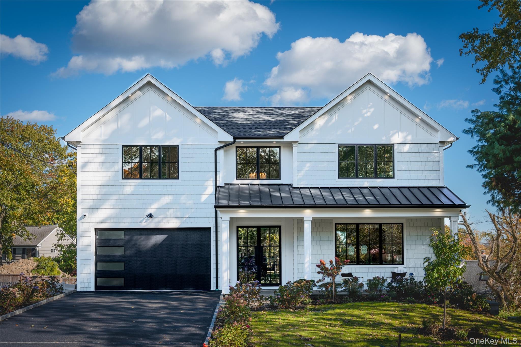 Modern inspired farmhouse with a standing seam roof, a metal roof, a front lawn, driveway, and an attached garage