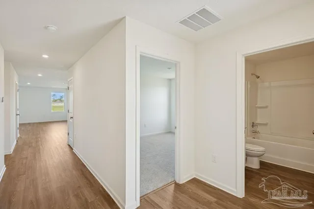 a view of a hallway with wooden floor and a bathroom