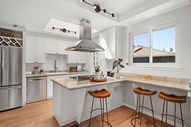 a kitchen with stainless steel appliances a stove a sink a refrigerator and chairs with wooden floor