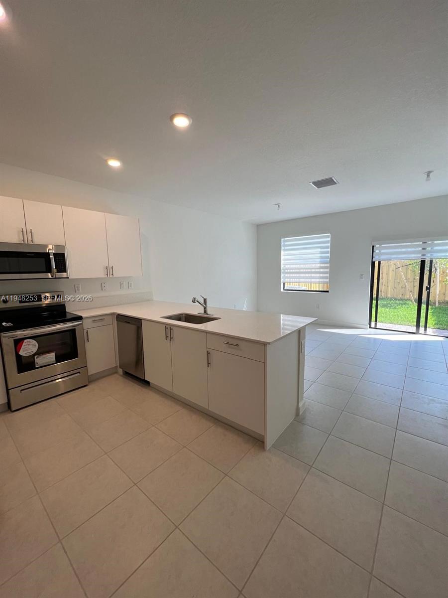 12908 Southwest 233rd Terrace, Unit 12908 Homestead, FL 33032 - Photo 11 of 23 a kitchen with stainless steel appliances kitchen island granite countertop a stove a sink and a refrigerator