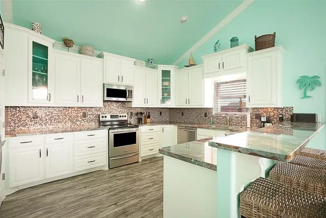 a kitchen with granite countertop a stove a sink and white cabinets