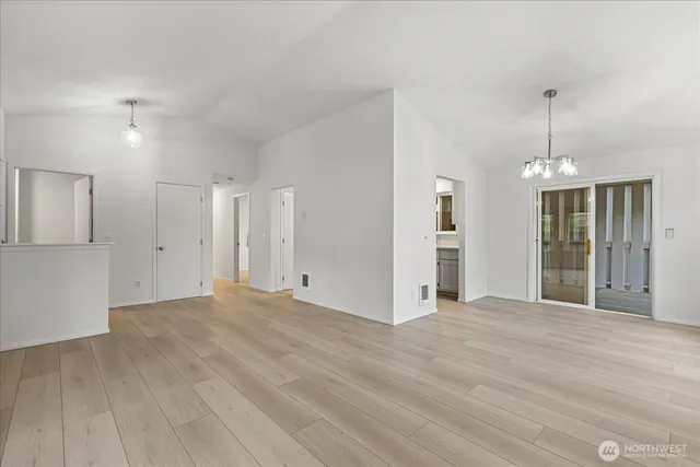 a view of an empty room with wooden floor and a kitchen