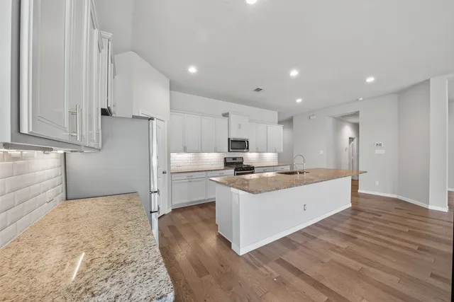 a large white kitchen with a stove a sink dishwasher and a refrigerator with wooden floor