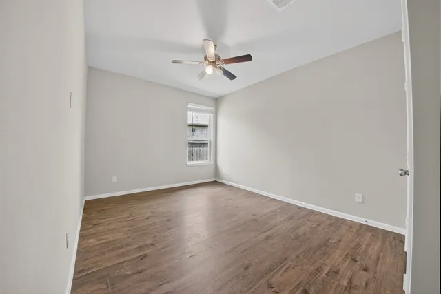 an empty room with wooden floor ceiling fan and windows