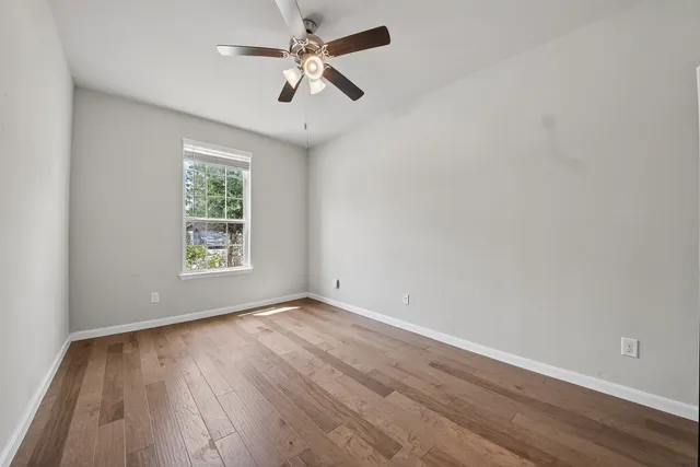 an empty room with wooden floor chandelier fan and windows