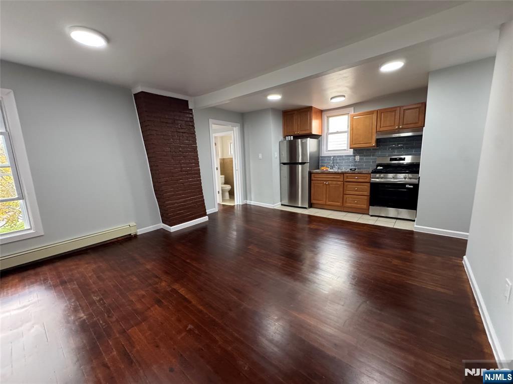 an empty room with wooden floor and entrance to kitchen