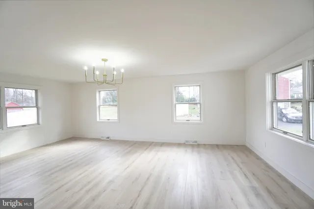 an empty room with wooden floor chandelier and windows