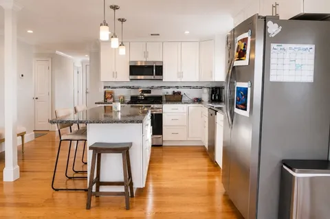 a kitchen with stainless steel appliances granite countertop a refrigerator a stove top oven a sink dishwasher and a refrigerator with wooden floor