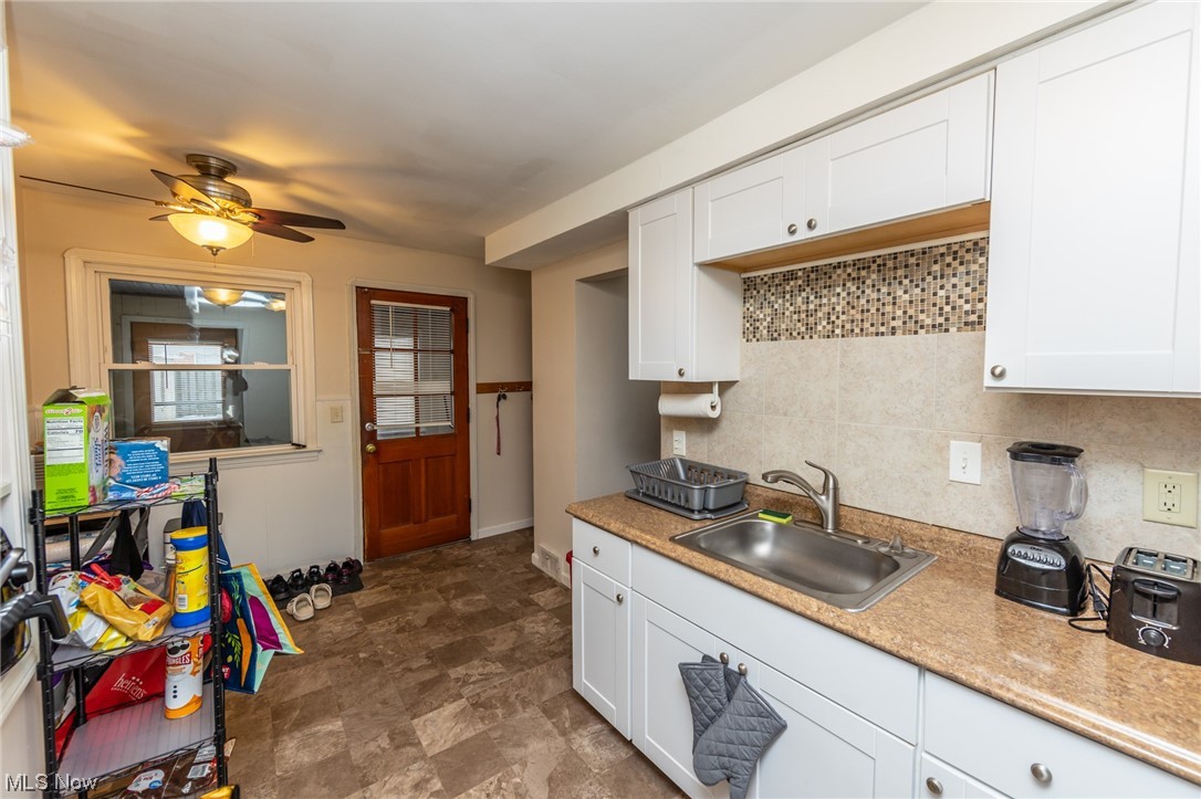 7433 Pearl Road Cleveland, OH 44130 - Photo 10 of 28 Kitchen with backsplash, light countertops, white cabinetry, ceiling fan, and vinyl floors