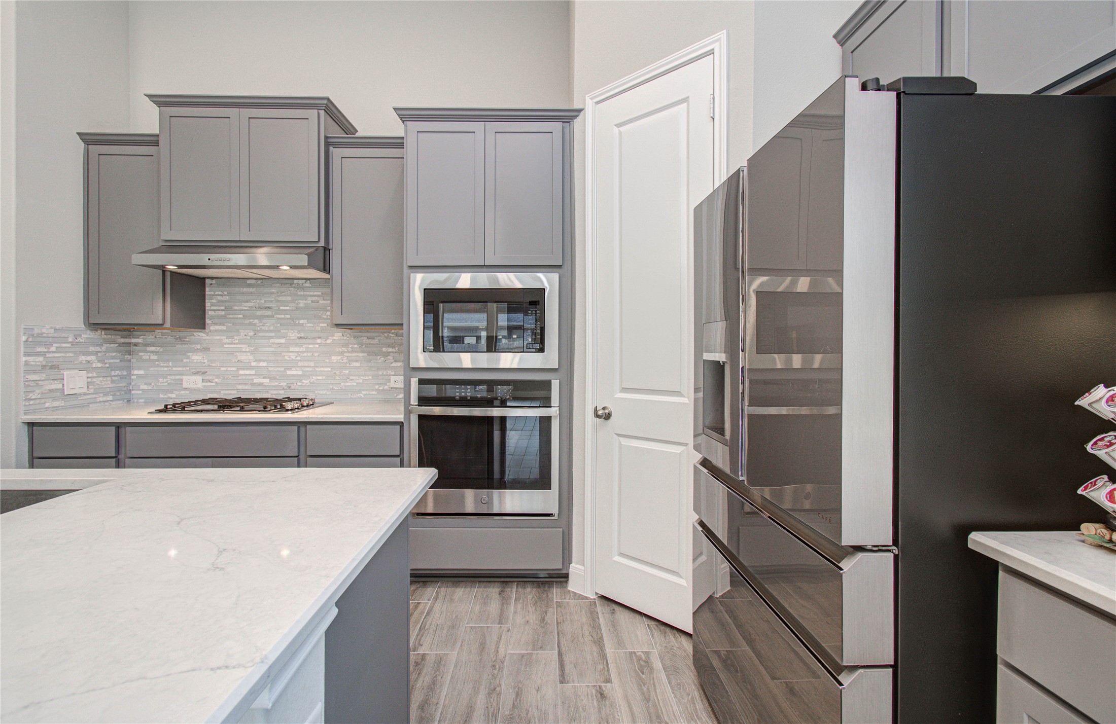 17344 Grand Canyon Road Conroe, TX 77302 - Photo 20 of 49 This modern kitchen features sleek gray cabinets, stainless steel appliances, and a stylish tile backsplash. The countertops are a clean white, complementing the wood-look flooring for an elegant and contemporary feel.