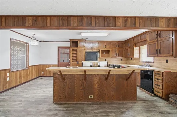 a living room with stainless steel appliances kitchen island granite countertop a refrigerator a sink dishwasher a stove and a dining table with wooden floor