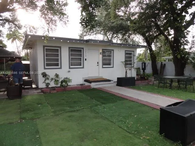 a backyard of a house with table and chairs potted plants and a large tree