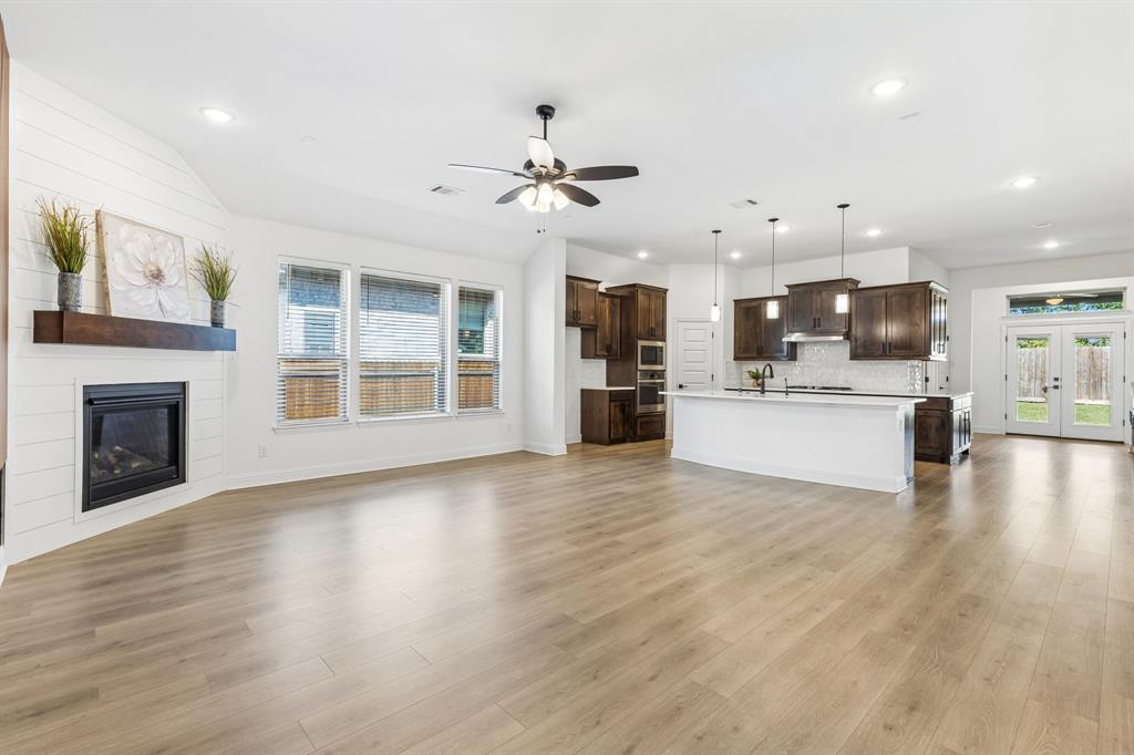 5224 Troupe Road McKinney, TX 75071 - Photo 7 of 31 Spacious room featuring wood-finish flooring, a fireplace with a wood mantel, a kitchen island with pendant lighting, dark wood cabinetry, and double glass-paneled doors