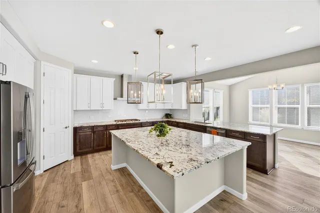 a kitchen with stainless steel appliances granite countertop stove top oven a refrigerator a sink and white cabinets with wooden floor