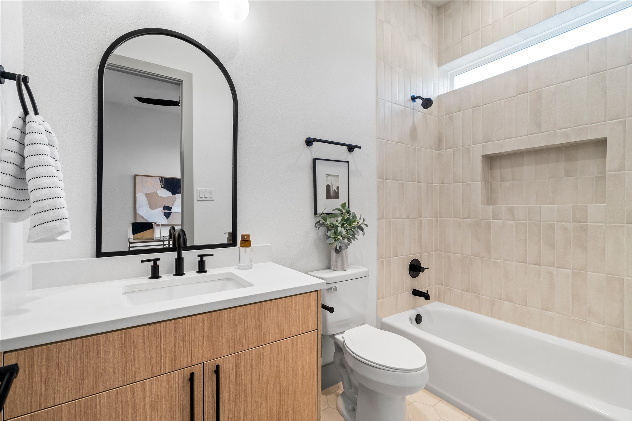 2950 Pitzlin Street Houston, TX 77023 - Photo 28 of 37 A beautifully appointed secondary bathroom with designer touches at every turn—featuring a floating wood vanity, quartz countertop, and a textured vertical tile surround with built-in niche. Matte black hardware and an arched mirror add a bold, modern edge to this serene and functional space.