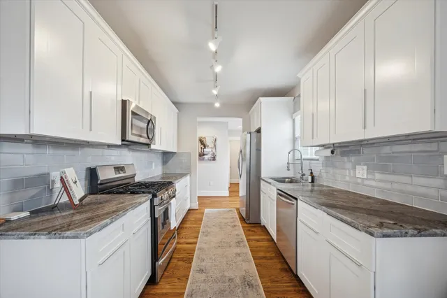 a kitchen with stainless steel appliances granite countertop wooden cabinets a sink a stove a dining table and chairs