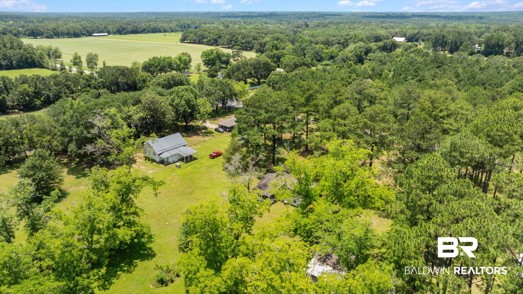 20540 Lacey Road Silverhill, AL 36576 - Photo 36 of 40 Expansive acreage featuring a white residence with a dark roof and a front porch, surrounded by lush green foliage