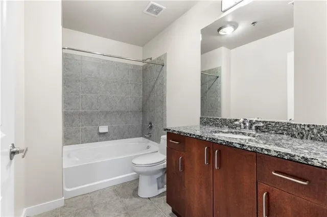 a bathroom with a granite countertop bathtub shower sink vanity and toilet
