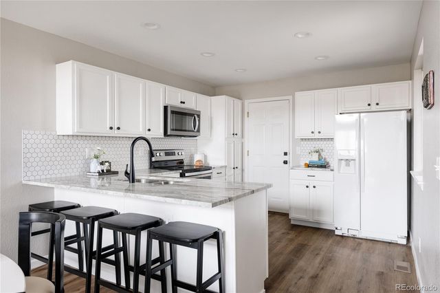 a kitchen with a refrigerator a stove a sink and white cabinets with wooden floor
